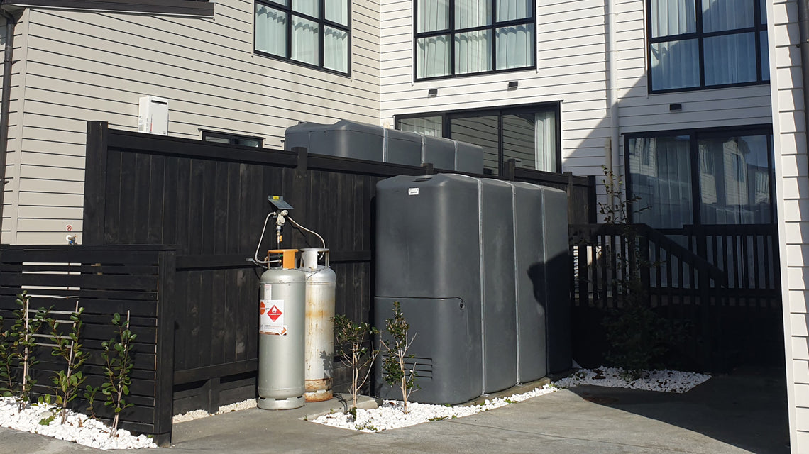 Promax slimline water tanks installed along a boundary fence between modern New Zealand townhouses