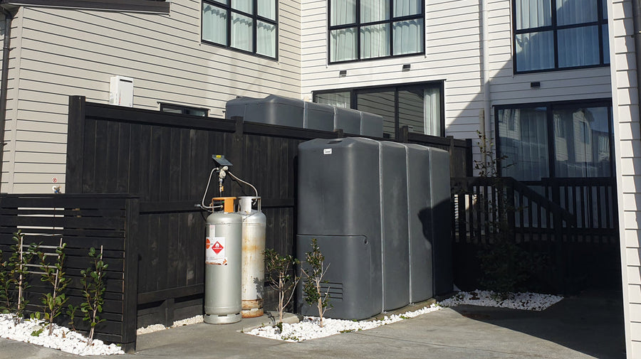 Promax slimline water tanks installed along a boundary fence between modern New Zealand townhouses